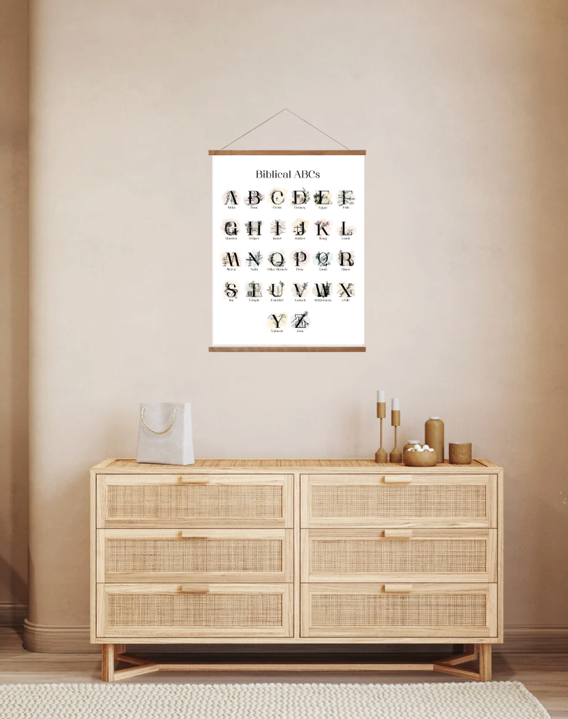 A wall poster hanging over a dresser, featuring the Christian alphabet with each letter paired with a biblical word, in a room with neutral decor.