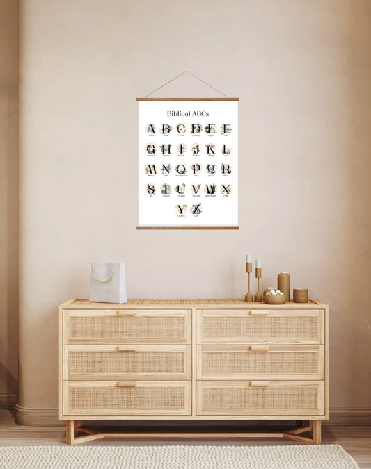 A wall poster hanging over a dresser, featuring the Christian alphabet with each letter paired with a biblical word, in a room with neutral decor.